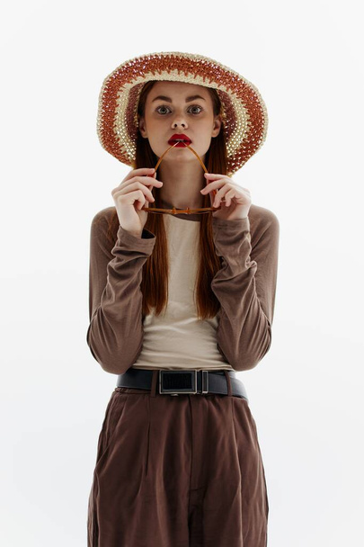 Una linda modelo de moda en un sombrero posa sosteniendo gafas sobre un fondo blanco. Catálogo de fotografía para la revista. Foto de alta calidad - Foto, Imagen