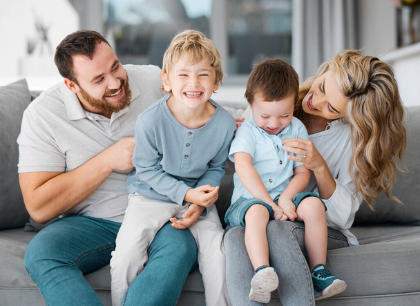 Carefree loving parents tickling and bonding with cute little laughing sons. Smiling caucasian family of four relaxing on the sofa at home.Playful young boys spending quality time with mom and dad. - Fotografie, Obrázek