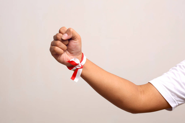Hand's man holding indonesian flag with red whit ribbon on the wrist. Isolated on gray background - Photo, Image
