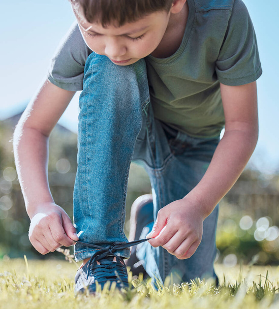 I can tie my own laces, whats next. an adorable little boy tying his shoelaces outside - Photo, image