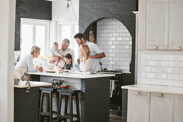 . Multi-generation caucasian family baking together in kitchen. Happy extended family baking a cake with ingredients on a table at home. Little girl baking with her parents and grandparents - Valokuva, kuva