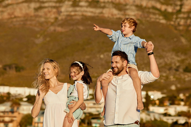 Carefree caucasian family walking and having fun together outside in summer. Parents carrying their daughter and son on holiday. Little siblings relaxing with their parents on vacation. - Zdjęcie, obraz
