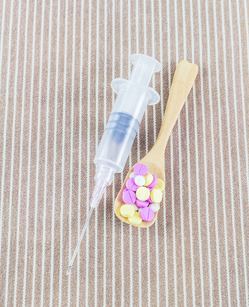 Jeringa con aguja y diferentes píldoras en cuchara de madera
 - Foto, imagen