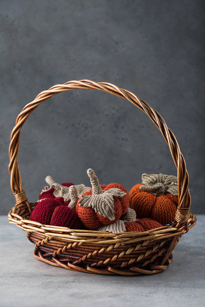 A bunch of knitted handmade pumpkins in a basket on a gray background. The concept of autumn and coziness. DIY decor. - Foto, afbeelding