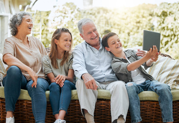 Toinen selfie isoäidit jääkaappi. nuori poika, joka käyttää digitaalista tablettia istuessaan kotona sisarensa ja isovanhempiensa kanssa - Valokuva, kuva