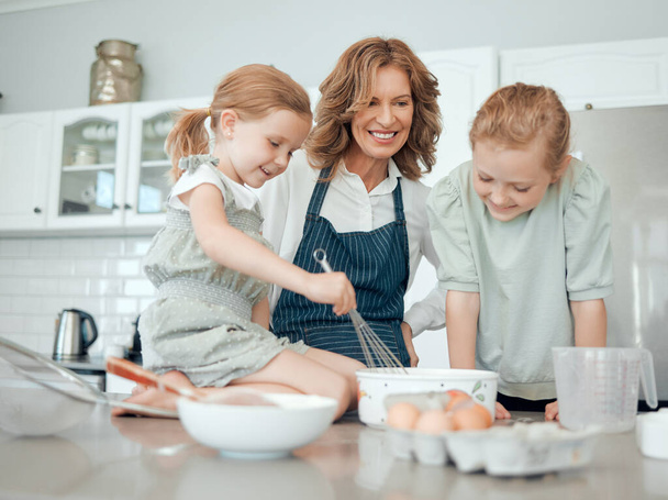 Everyone gets a turn to whisk. a grandmother baking with her two granddaughters at home - Foto, Bild