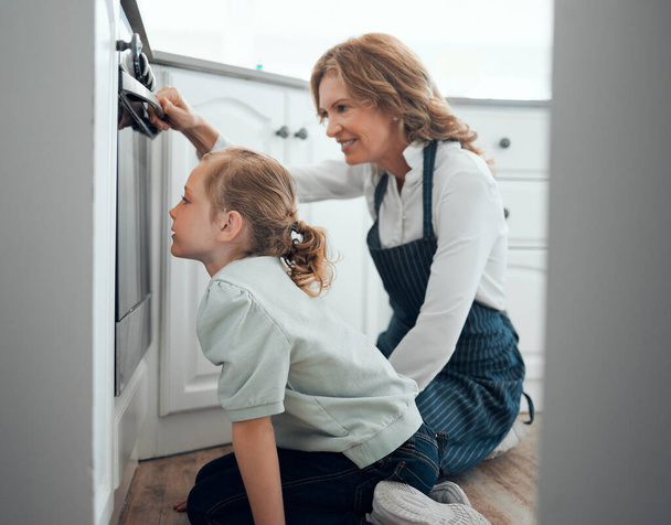 Its baking well in there. a grandmother and her granddaughter checking what is baking in an oven at home - Foto, imagen
