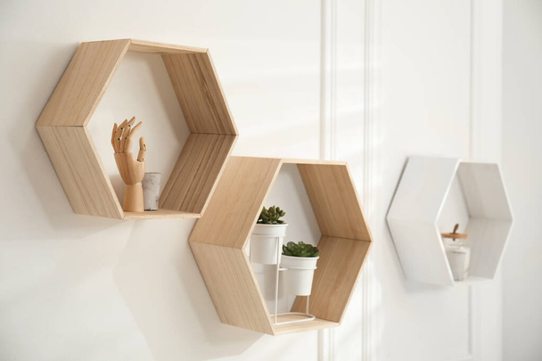 Honeycomb shaped shelves with decorative elements and houseplants on white wall - Фото, зображення