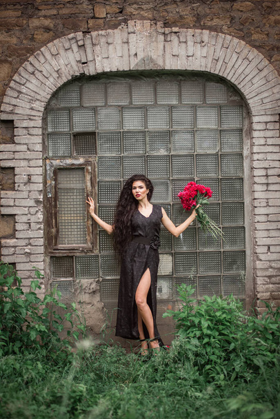schöne junge Frau in einem schwarzen Kleid und einem roten Rock auf dem Hintergrund einer Backsteinmauer - Foto, Bild