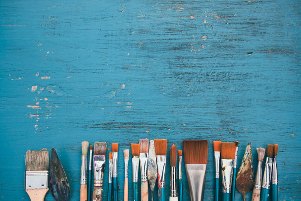 Artistic art supply utensils with paintbrushes on turquoise wooden background with copy space. Flat lay photo - Foto, Imagen