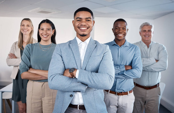 Believing in yourself is the first secret for success. Portrait of a confident young businessman standing with his arms crossed in an office with his colleagues behind him - Photo, Image