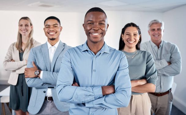 Your energy introduces you before you even speak. Portrait of a confident young businessman standing with his arms crossed in an office with his colleagues behind him - Foto, Imagen