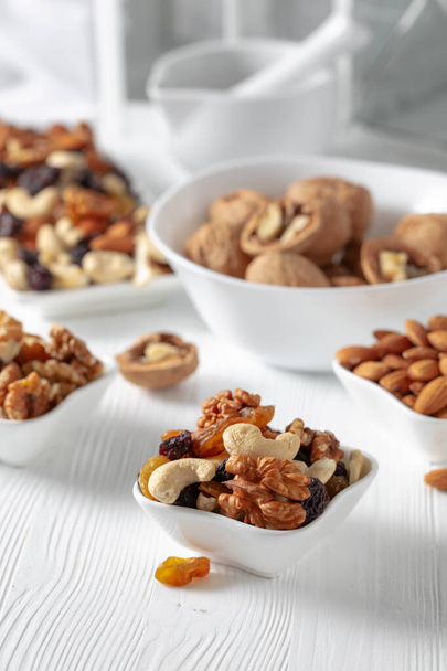 Mix of nuts and raisins on a white wooden table. Presented raisins, walnuts, hazelnuts, cashews, pecans, and almonds. - Photo, Image