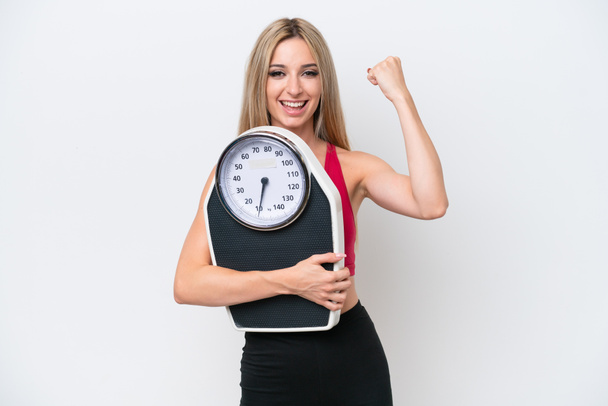 Pretty blonde woman isolated on white background with weighing machine and doing victory gesture - Photo, Image
