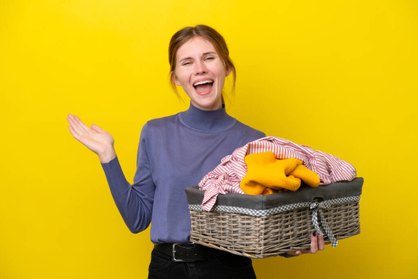 jonge Engels vrouw met een kleding mand geïsoleerd op gele achtergrond met geschokt gezicht expressie - Foto, afbeelding