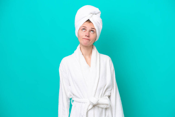 Young woman in a bathrobe isolated on blue background and looking up - Foto, Imagen