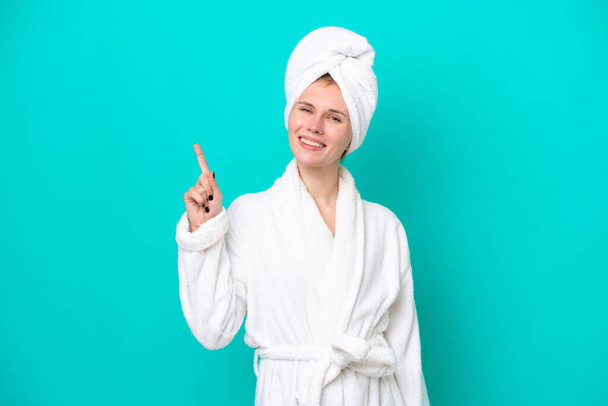 Young woman in a bathrobe isolated on blue background showing and lifting a finger in sign of the best - Foto, immagini