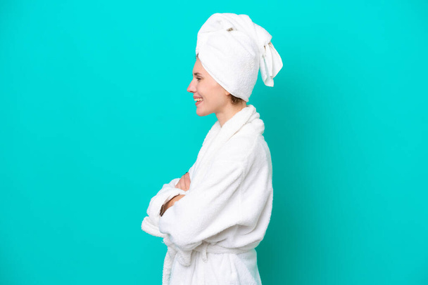 Young woman in a bathrobe isolated on blue background in lateral position - Foto, Imagem