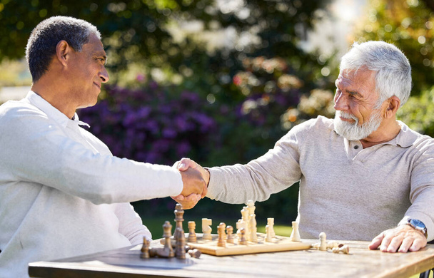 Gut gespielt. zwei Männer, die zusammen draußen sitzen und sich nach einer Schachpartie die Hände schütteln - Foto, Bild