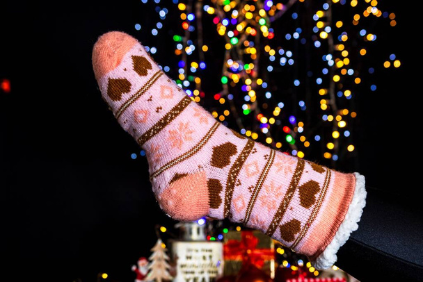 A close-up of a leg in Christmas sock against bokeh lights - Valokuva, kuva