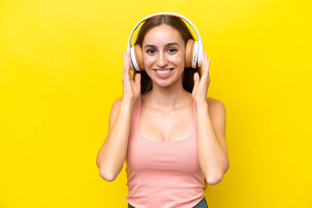 Joven mujer caucásica aislada sobre fondo amarillo escuchando música - Foto, Imagen