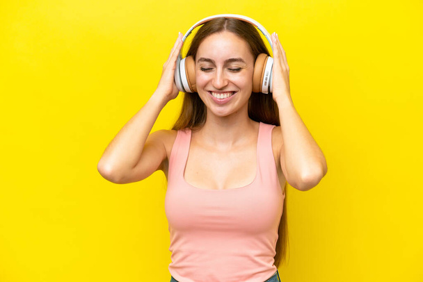 Young caucasian woman isolated on yellow background listening music - 写真・画像