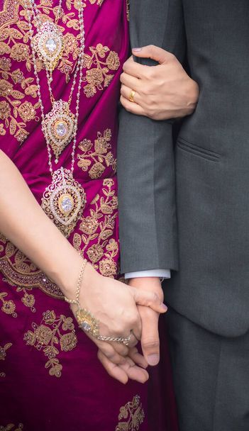 Bride holding groom's hand close up photo. Gold Jewelry and purple homecoming dress. - Фото, изображение