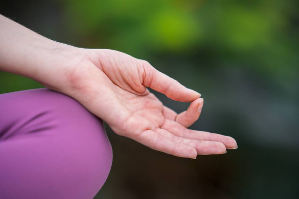 A hand on knee of Caucasian woman yogini meditating on a green blurred background - Photo, image