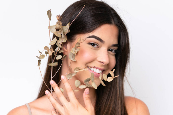 Young Brazilian woman isolated on white background holding a eucalyptus branch while smiling. Close up portrait - Foto, afbeelding