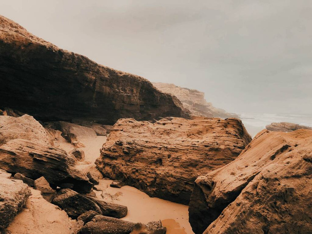 Rocky cliffs on a beach over a background of a cloudy sky - Φωτογραφία, εικόνα