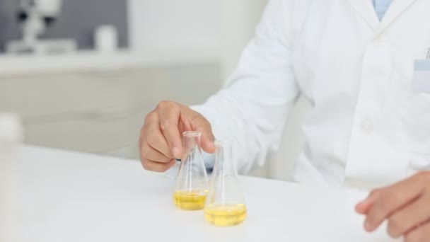 Closeup hands of a scientist conducting an experiment with yellow liquid in a research laboratory. Researcher mixing sample in beakers in a chemical or science lab. Doing an experiment to find a cure. - Video, Çekim