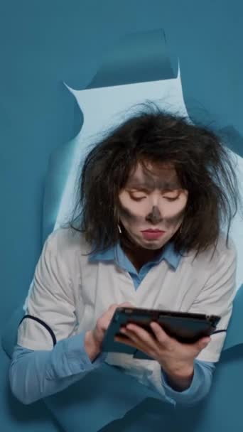 Vertical video: Crazy insane chemist with messy hair using digital tablet and browsing internet, feeling mad funny and doing goofy expressions. Foolish amusing female scientist having wacky grimace. - Materiaali, video