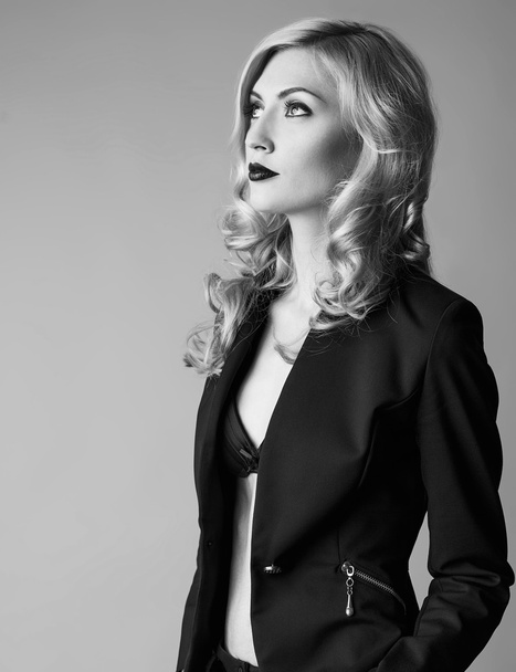 Young blond sexy woman in a business suit on a grey background.  - Valokuva, kuva