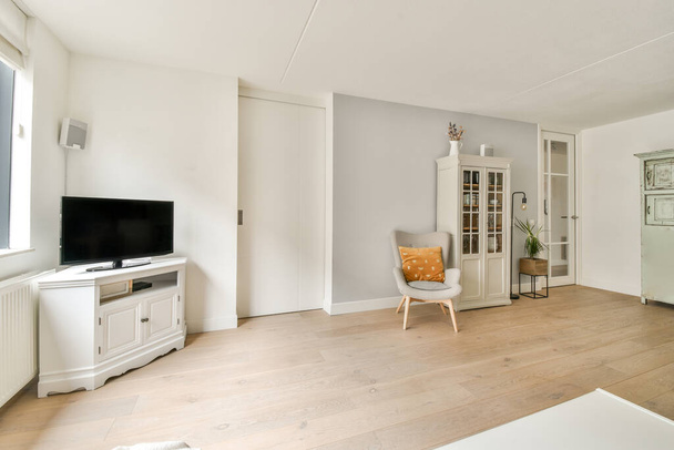 Současný minimalistický design interiéru světlého studiového bytu s dřevěným stolem a židlemi v jídelně mezi otevřenou kuchyní a obývacím pokojem s bílými stěnami a parketovou podlahou - Fotografie, Obrázek