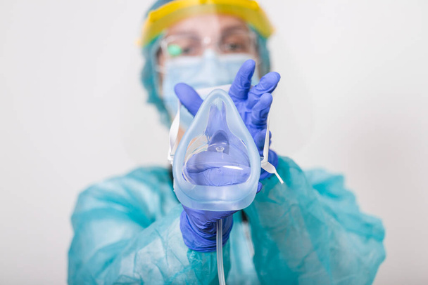 Arzt hält Sauerstoffmaske hoch, als wolle er Patient im Krankenhaus anziehen, Mitarbeiter des Gesundheitswesens bei der Coronavirus-Covid19-Pandemie in Schutzausrüstung setzen Sauerstoffmaske auf - Foto, Bild