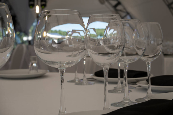 Close up clean empty wine glasses on white served dinner table in party tent on summer sunny day.Concept of party planning manager services. Tableware shop window. Design pattern for glass packaging - Foto, Bild