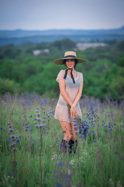 young beautiful girl in a hat and a white dress walks in the field of a flowering lavender. - Fotografie, Obrázek