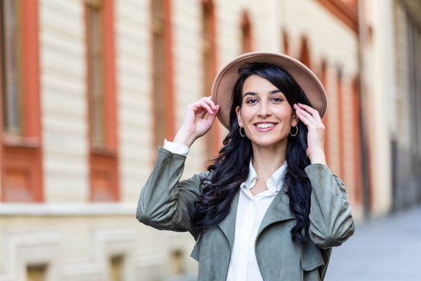Outdoor portrait of a young beautiful fashionable happy lady posing on a street of the old city. Model wearing a hat. Girl looking up. Female fashion. City lifestyle. Copy space for text - Fotó, kép