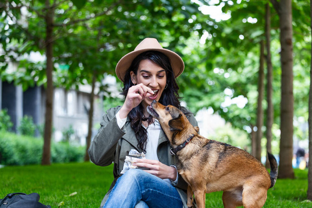 Güzel, genç bir kadın köpeğiyle dışarıda parkta oynuyor. Yaşam tarzı portresi. Sevimli genç bir kadın yavru köpeğini kucaklıyor. Sahibi ve köpeği arasında aşk. - Fotoğraf, Görsel