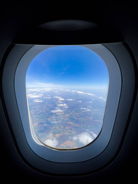 View from airplane window. Bull's eye view on beautiful sky, black background. Air travel concept: Looking out aircraft bull's eye. Beautiful scenery from the air through plane porthole.  - 写真・画像