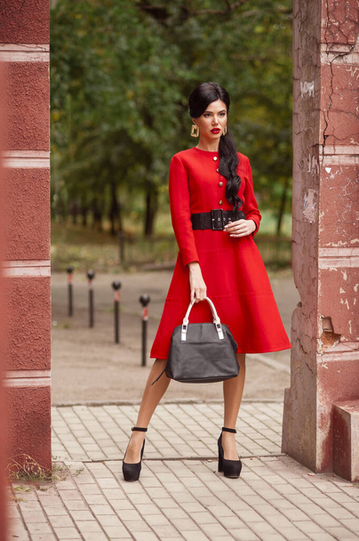 schöne junge Frau in rotem Kleid und schwarzem Rock und Mantel, die auf der Straße läuft - Foto, Bild
