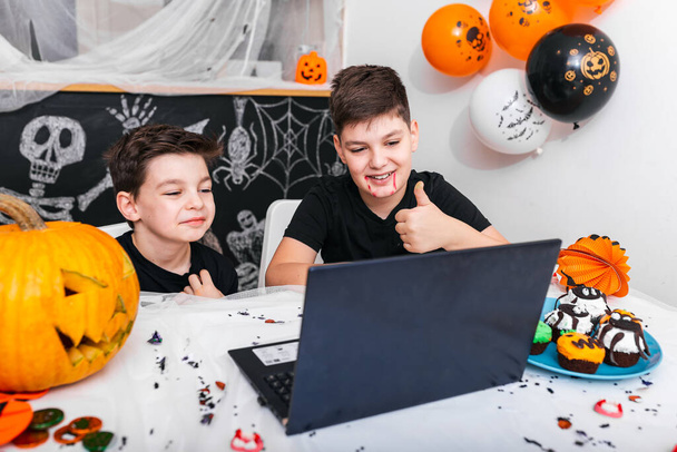 Happy young boys, brothers talking with grandparents or friends via video call using laptop on halloween day , excited boys in costumes looking at computer showing thumbs up - Foto, imagen