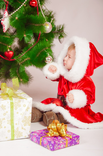Baby in Santa costume at the Christmas tree with gifts - Fotó, kép