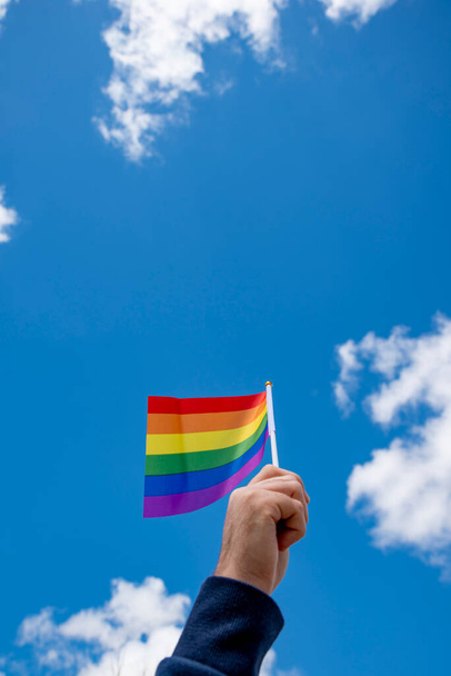 mano sosteniendo una bandera del arco iris Lgtb ondeando en un cielo azul. Movimiento Lgtb.  - Foto, Imagen