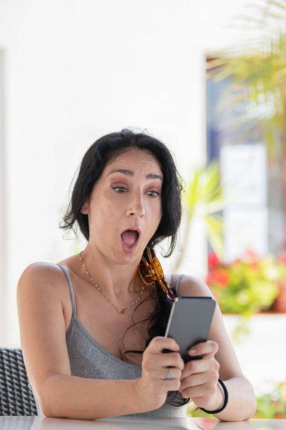Imagem vertical de uma mulher adulta espantada sentada em um café olhando seu telefone fora. Fcous selectivos. - Foto, Imagem