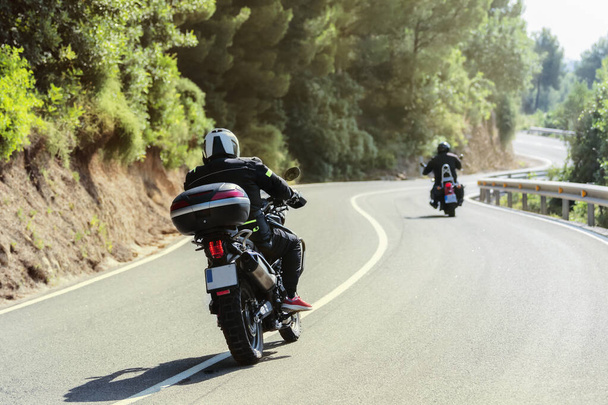 Biker in Motorradausrüstung fahren auf einer kurvenreichen Straße auf einem unscharfen Hintergrund. Selektiver Fokus. Fahr- und Freizeitkonzept. - Foto, Bild