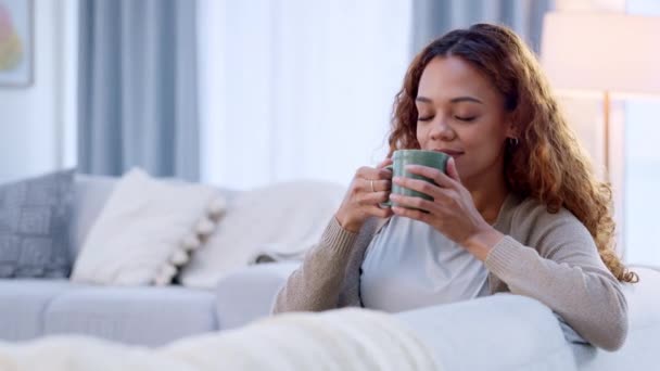 Relaxed woman drinking coffee and feeling carefree and refreshed while relaxing on the couch at home. Female taking deep breath and smelling the aroma of a hot beverage, feeling mindful and content. - Кадры, видео