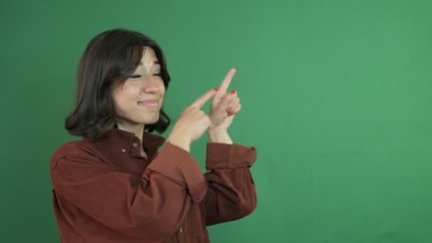 Ekranın köşesini parmaklarıyla gösteren bir kız resmi. Yeşil perdenin önündeki genç kadının yüz ifadesi. - Video, Çekim