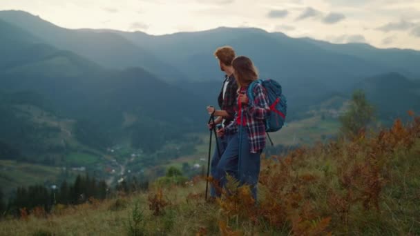 Sporty couple trekking hiking outdoors in mountains. Active family travel walk on green hill. Young tourists look picturesque landscape view together. Backpackers going on hike trail. Tourist concept. - Video