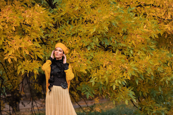 beautiful young woman in a black jacket and a hat with a yellow maple leaves in the autumn park - Valokuva, kuva